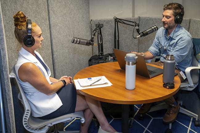 A Caucasian man and woman talking in a podcast studio for a podcast episode