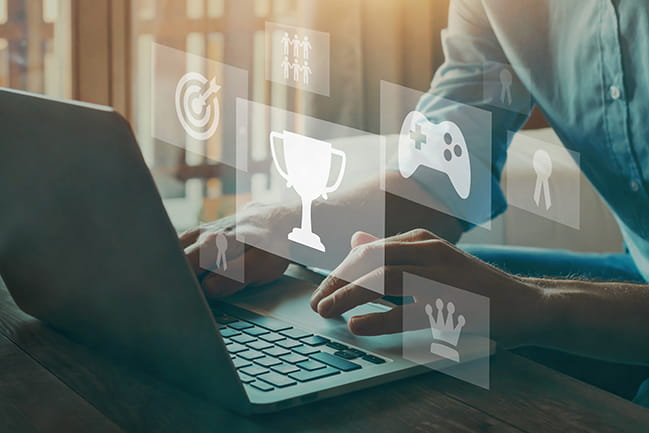 Caucasian man in front of laptop with game icons floating in front of him, over laptop.