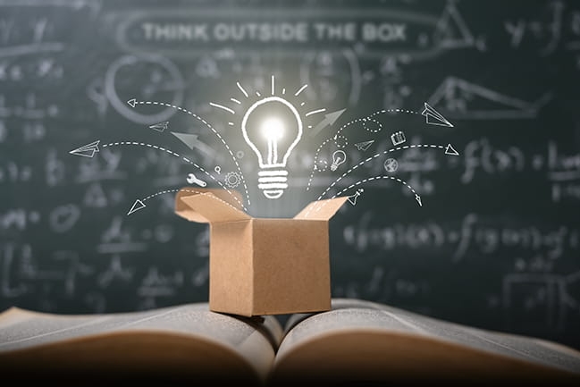 think outside the box on school green blackboard, box with floating, glowing lightbulb coming out of it, over open book