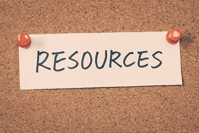 Piece of paper with "Resources" written on it, tacked to cork board with red pushpins