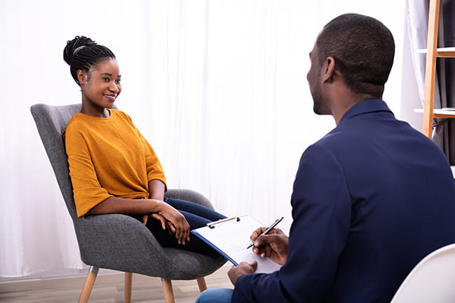 Young African Woman Sitting Near Psychologist With Clipboard To Treat Depression