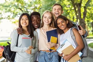Group of international happy students with books and notebooks having fun in park after studying, smiling at camera