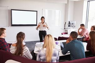 Female-presenting professor giving lecture in a university classroom