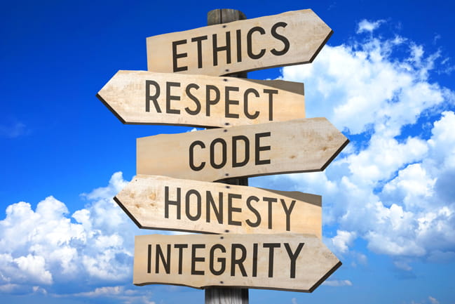 Wooden signpost with each post pointing in a different direction. Each post contains a word related to code of conduct (ethics, respect, code, honesty, integrity)