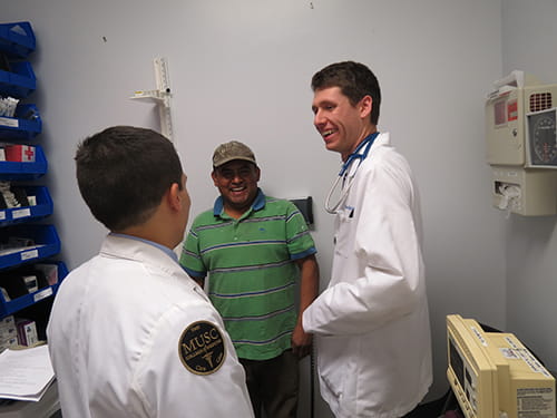 Two medical students laugh and talk with a patient
