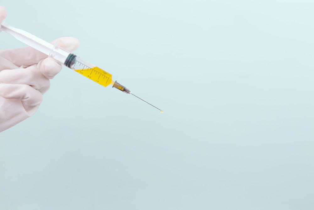 a gloved hand holding a syringe with yellow liquid inside