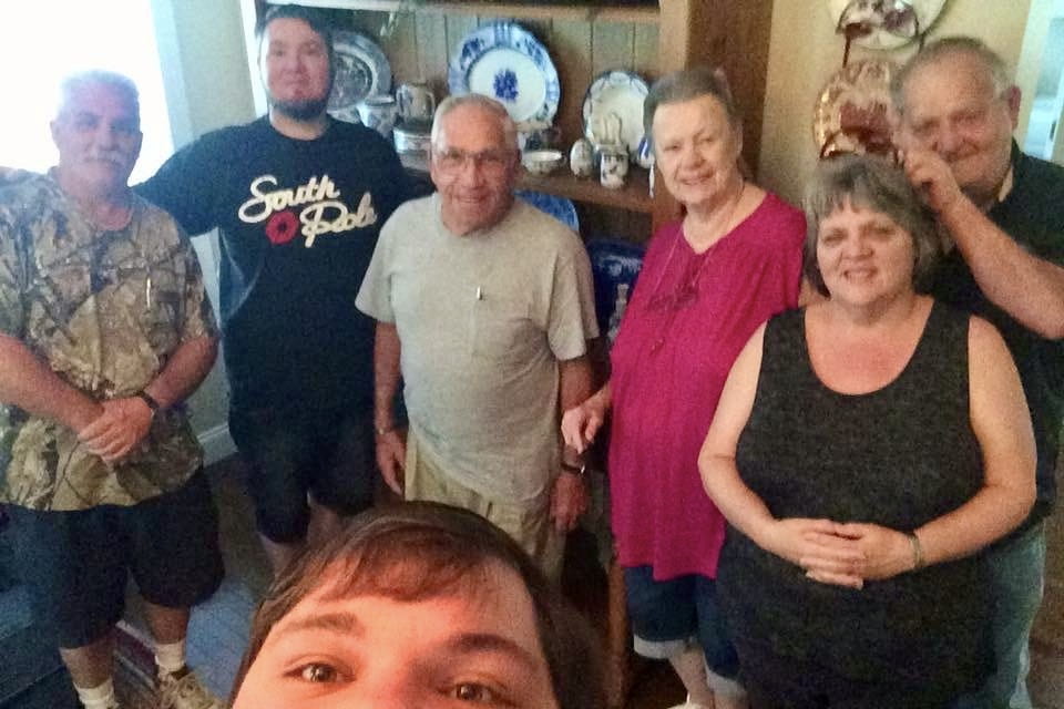 Casey Chubb in a selfie with six family members standing behind him