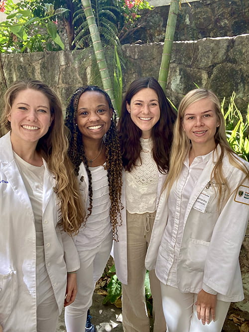 group shot of four young women wearing student white coats in a tropical setting