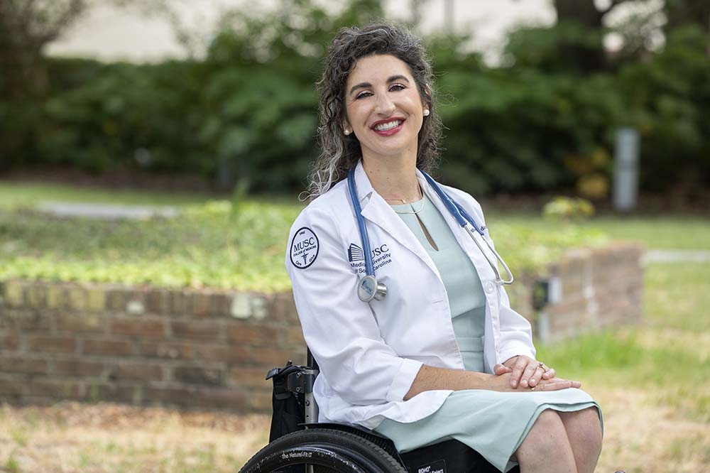 College of Medicine graduate Julia Rodes in her wheelchair wearing her white doctor's coat with a big smile on her face.