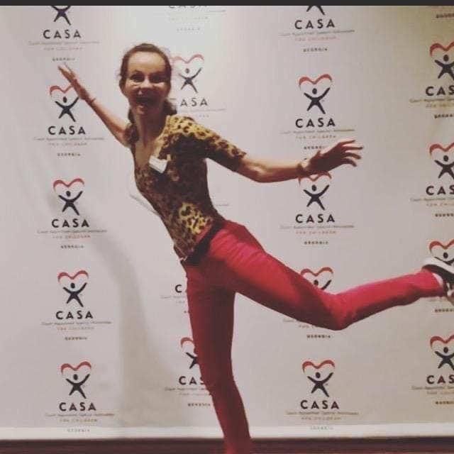 Crystal Wood balances on one foot, smiling, in front of a step and repeat with the words CASA on it
