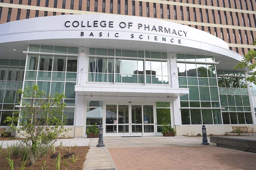 The words College of Pharmacy and Basic Science are on a white sweeping bar above a building with walls made of glass.