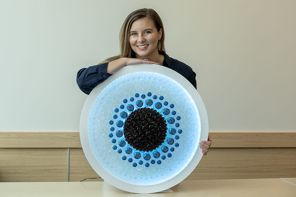 Smiling woman leans on a torso-sized circle that is filled with blue, darker blue and black lights.