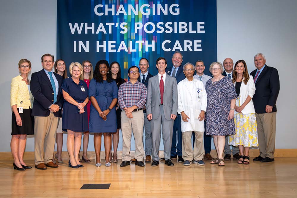 Group of people pose in front of sign that says Changing What's Possible in Health Care. They are wearing dress clothes.