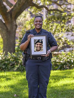 Woman in blue police uniform holds a picture of herself in military uniform.
