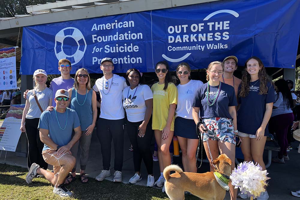 Young people in exercise clothes stand in front of a blue banner that says American Foundation for Suicide Prevention and Out of the Darkness Community Walks.
